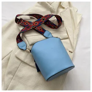 Detailansicht einer hellblauen Eimertasche aus Leder mit buntem Ethno-Webschultergurt