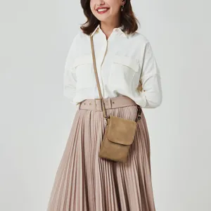 Model wearing a tan PU leather crossbody phone bag with a white shirt and pleated skirt.