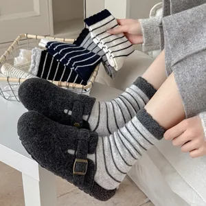 Nahaufnahme von gestreiften Wollsocken kombiniert mit grauen Pelz-Clogs.