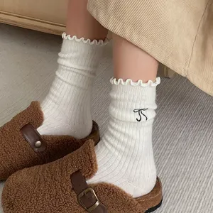 Chaussettes douillettes en laine blanche à volants délicats et broderie de nœud noir.