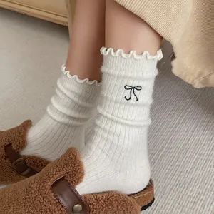 Vue détaillée de chaussettes en laine blanche avec poignets en dentelle et broderie de nœud.
