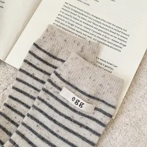 Close-up detail of striped wool socks featuring a minimalist 'egg' embroidered label