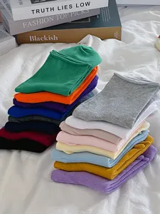 Detail view of colorful rolled cuff socks stacked neatly on white bedding, cozy lifestyle style.