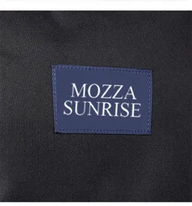 Close-up of MOZZA SUNRISE logo patch on durable black fabric of lightweight backpack