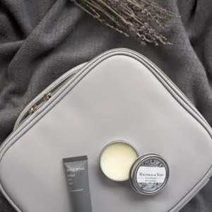 Detalle del neceser de cuero PU gris con textura de grano cruzado y accesorios de viaje.