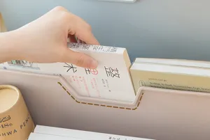 Vista dettagliata di una mano che mette un libro in un organizer da scrivania rosa inclinato