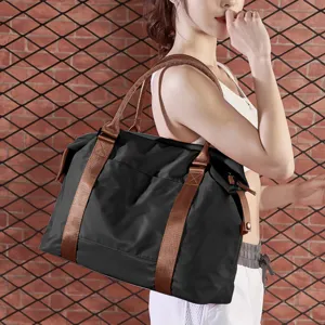 Large black travel gym bag with durable brown handles carried by a female model