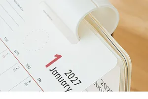 Dettaglio ravvicinato delle pagine del calendario da tavolo 2027 con clip in plastica.