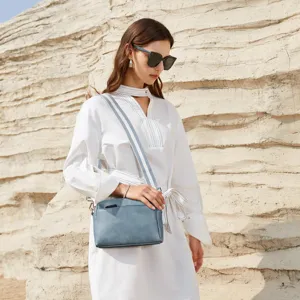 Bolso bandolera pequeño de piel azul con tres cremalleras y correa a rayas en modelo