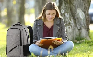 Grauer Laptop-Rucksack neben einer Frau, die im Freien in einem Park liest.