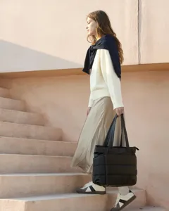 Detail of a woman holding a large black quilted tote bag while walking upstairs