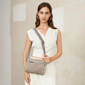 Primer plano de un bolso bandolera de cuero gris con correa ancha estampada en una modelo.