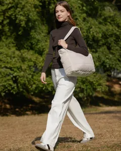 Stylish model carrying a large beige quilted tote bag in a sunny outdoor garden.