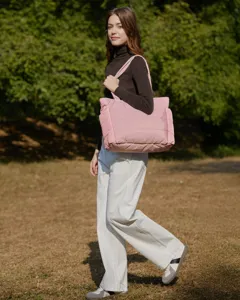 Detail view of a large pink quilted tote bag carried by a model outdoors in a park.