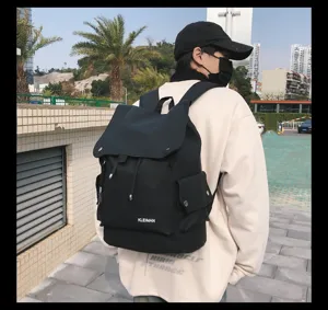 Detail of a black waterproof large-capacity flap-over backpack worn by a model outdoors.