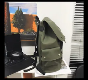 Side detail view of a minimalist olive green waterproof backpack on a desk with a laptop