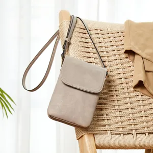 Detail view of a taupe PU leather crossbody phone bag hanging on a woven chair