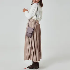 Close-up of a stylish mauve PU leather phone bag worn by a model over a pleated skirt.