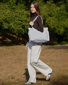 Stylish large light blue quilted tote bag carried by a fashion model in a sunlit park