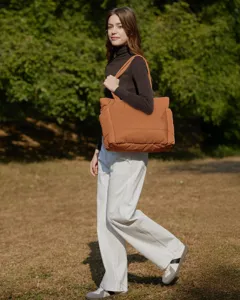 Female model carrying a large orange quilted tote bag in a sunny outdoor park setting.