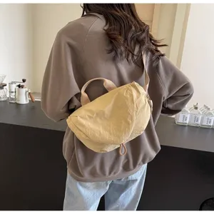 Back view showing the fit and scale of a beige nylon crescent dumpling bag on a model