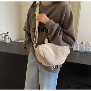 Close-up detail of a minimalist cream nylon crossbody dumpling bag on model's shoulder