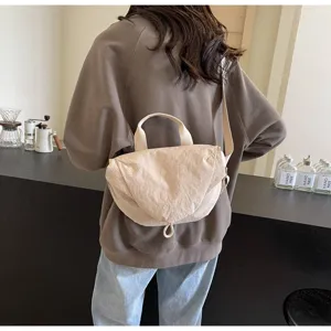 Close-up back view of a beige nylon dumpling crossbody bag worn by a person in a casual setting