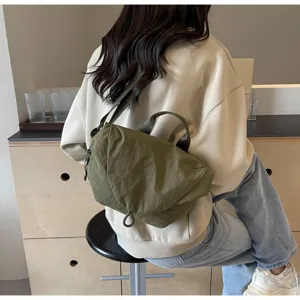 Detail view of an olive green nylon crossbody bag worn on the back of a sweatshirt.