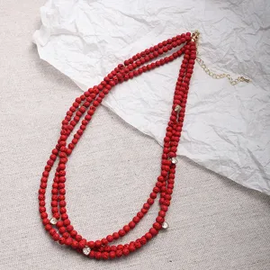 Detalle de un collar de tres capas de cuentas rojas con pequeños dijes de corazón de cristal