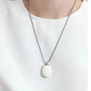 Detailed close-up of a minimalist white enamel pebble pendant necklace on a model