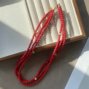 Primer plano de un collar de tres hileras de piedra de erizo rojo con dijes de corazón