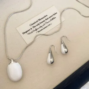 Close-up of minimalist white enamel and silver-plated necklace with matching drop earrings.