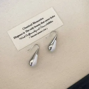 Elegant close-up of minimalist white enamel and silver-plated teardrop drop earrings