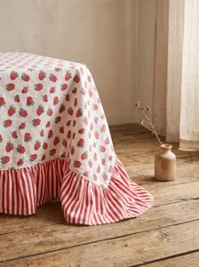 Detail of pastoral tablecloth featuring red strawberry prints and striped ruffled edge