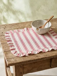 Close-up detail of red striped placemat with elegant ruffles on a rustic wooden table surface