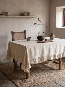 Dettaglio della tovaglia in cotone lavato beige con bordi a balze su tavolo
