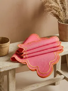 Detail view of pink scalloped embroidered linen placemat on a rustic wooden bench