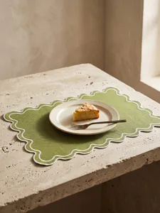 Detail of green scalloped embroidered placemat with cake plate on a stone table