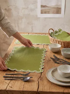 Detail shot of green scalloped embroidered placemat on a rustic wooden dining table.