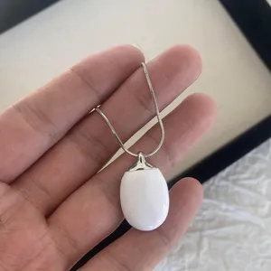 Close-up of a minimalist white enamel oval pendant necklace on a silver-tone chain