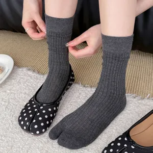 Detailed shot of women's grey ribbed split toe socks paired with black polka dot tabi shoes.