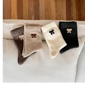 Detalle de cuatro pares de calcetines de algodón suave en colores neutros con lazos bordados.
