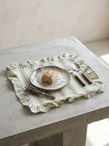 Detail view of rustic green striped linen placemat with ruffled edge on a stone table