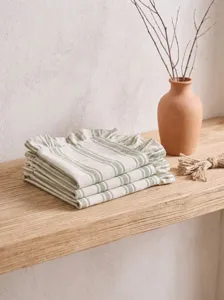 Detailed view of green striped ruffled linen napkins neatly folded on a rustic shelf