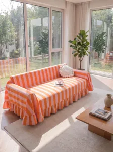 Modern orange and pink striped sofa cover with elegant ruffles in a sunlit living room decor