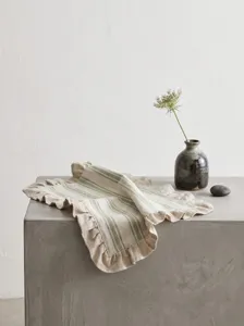 Close-up of ruffled edge linen placemat with green stripes on a concrete table