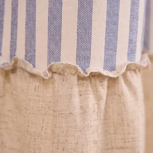 Détail macro du rideau en lin beige et rayé bleu avec une finition couture à volants