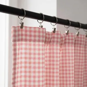 Detalle de cortinas de algodón y lino a cuadros rosas colgadas de una barra negra con clips