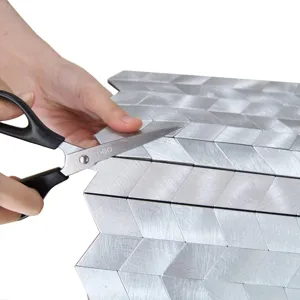 Vista de cerca cortando azulejos de mosaico de metal plateado con unas tijeras
