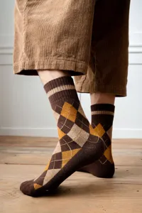 Detailed view of warm brown argyle patterned mid-calf socks for men worn on a wooden floor